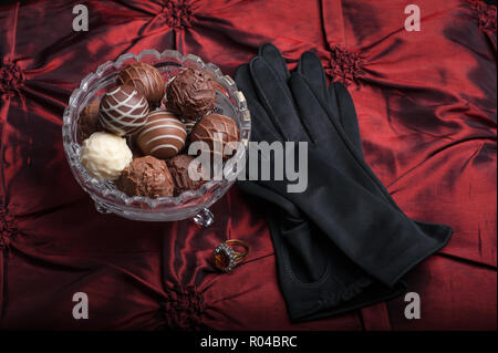 Schokolade Trüffel auf rotem Hintergrund mit schwarzen Handschuhen und Ring. Stockfoto