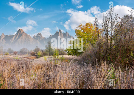 Spätherbst frostigen Tag zusammengesetzte Bild. Hohe Gras und Bäume im Herbst Laub. Berge mit hohen Gipfeln in der Ferne unter einem strahlend blauen Himmel mit Stockfoto