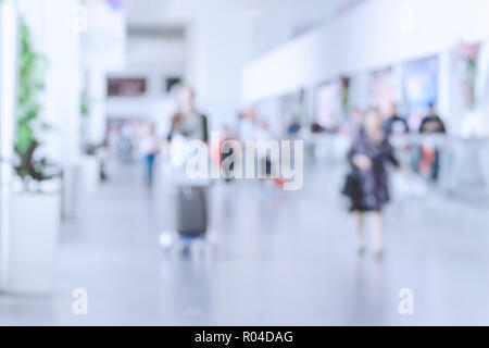 Verschwommenes Foto mit Menschen am Flughafen, defokussierten Silhouetten in Innenräumen, unerkennbare Personen, abstrakten Hintergrund mit Masse, Bewegungsunschärfe. Stockfoto