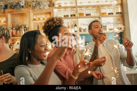 Diverse Freunde lachen und feiern mit Wunderkerzen in einer Bar Stockfoto