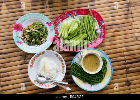 Traditionelle thailändische pikante Mittagessen mit Huhn, Reis, Gemüse und Soße auf einer Bambus Matte Stockfoto