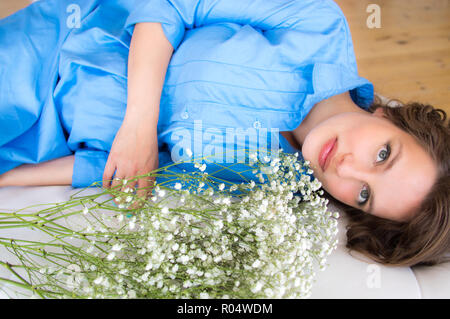 Schwangere Frau im blauen Kleid liegt auf runden Sofa mit Blumenstrauß Stockfoto