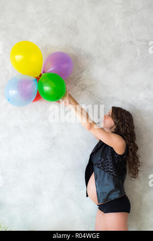 Schwangere Frau mit Luftballons in den Händen, graue Wand im Hintergrund Stockfoto