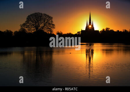 02/11/18 Vor einer kalten Nacht, die Sonne scheint durch die zentralen Turm der Kathedrale von Lichfield, und ist in Stowe Pool wider. Die Staffordshire mittelalterliche Kathedrale ist die einzige englische Kathedrale mit drei Türmen. Die drei Türme werden oft als die Damen der Vale' bezeichnet. Stockfoto