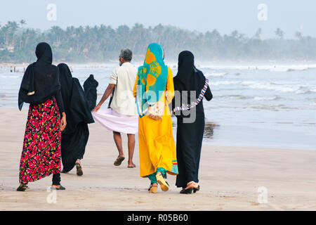 Muslimische Frauen am Strand entlang, ein Mann vor. Ansicht von der Rückseite. Sri Lanka. Stockfoto