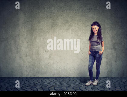 Junge Brünette in lässigen Jeans und T-Shirt auf grauen Hintergrund lächelnd an Kamera Stockfoto