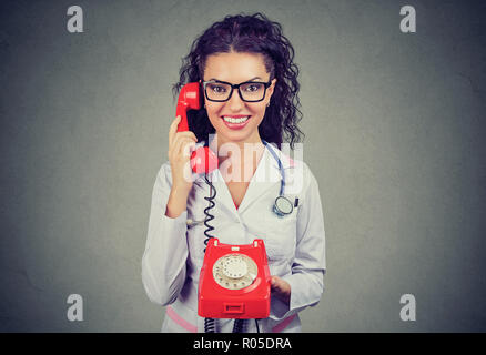 Fröhliche Brünette in Gläsern tragen weiße Mantel mit Stethoskop und halten roten retro Telefon lächeln an Kamera Stockfoto