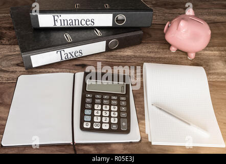 Finanzen und Steuern Konzept mit Ringbücher, Sparschwein und Rechner auf hölzernen Tisch Stockfoto