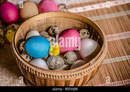 Weiß frisches Huhn Eier, Wachteleier mit bemalten Ostereiern und einem Spielzeug gelb tsiplenok in einem Strohkorb liegen auf einem Stroh Teppich Stockfoto