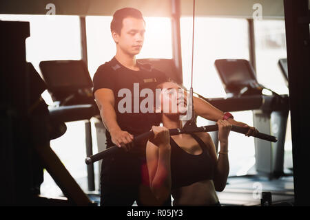 Junge fitness asiatische Frau ausführen mit Übung - Maschine mit einem persönlichen Trainer im Fitnesscenter. Fitness, Bodybuilding, Bewegung und gesunde Lebensweise. Stockfoto