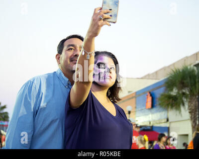 Eine Frau Gesicht Farbe tragen, und ein Mann ein smart phone selfie zusammen an die 2018 Dia de Los Muertos Feier in Corpus Christi, Texas USA. Stockfoto