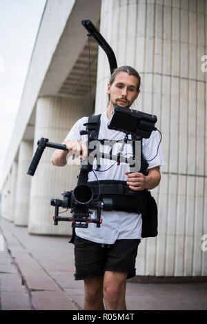 Professionelle Videofilmer holding Kamera auf 3-Achs Gimbal, die auf einfache Rig montiert. Videofilmer mit Steadicam. Pro Ausrüstung hilft Video in hoher Qualität ohne Schütteln zu machen. Stockfoto