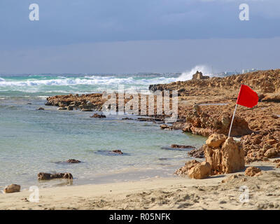 Rote Warnlampe Flagge auf einem steinigen Strand bei einem Sturm mit dem Brechen der Wellen Stockfoto