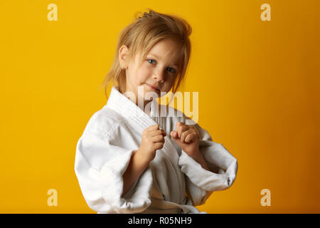 Kaum ernsthaft Mädchen tragen weiße Fighter Kimono und in Pose auf gelbem Hintergrund Stockfoto