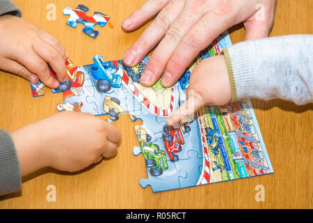 Kleine Kinder mit Rätseln auf hölzernen Tisch spielen zusammen mit Eltern, Lifestyle Menschen Konzept Stockfoto