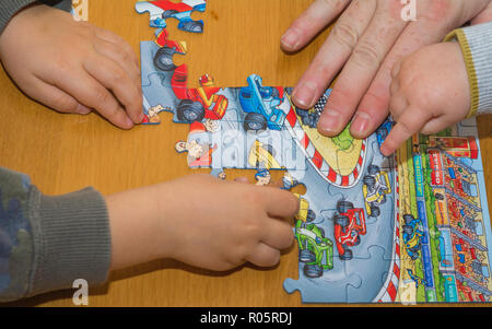 Kleine Kinder mit Rätseln auf hölzernen Tisch spielen zusammen mit Eltern, Lifestyle Menschen Konzept Stockfoto