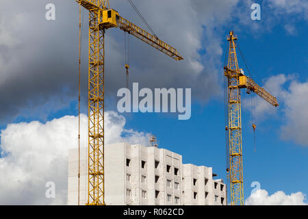 Eine große Anzahl von gelben Baukränen während der Konstruktion und dem Bau eines mehrstöckigen Wohnhaus mit Wohnungen für Mitarbeiter Stockfoto