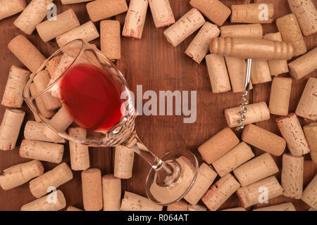 Ein Foto von einem Glas Rotwein mit Korken und ein Vintage Korkenzieher auf einem dunklen Holzmöbeln im Landhausstil Hintergrund, getönten Bild. Eine Weinprobe Einladung Stockfoto