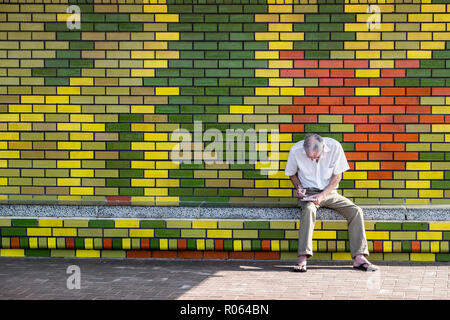 Eine ältere europäische männlich Scribbles, einige Notizen auf der Bank vor der bunten Wand der Marine Surf Lifesaving Club. Durban Beachfront, Stockfoto