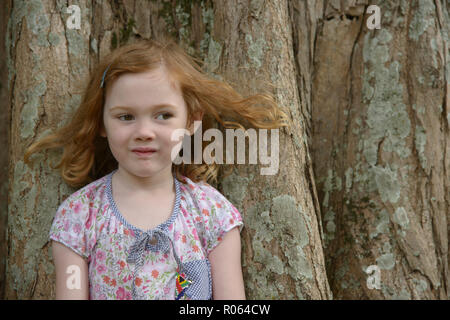 Eine junge Rothaarige kaukasische Mädchen steht mit dem Rücken gegen einen großen Baum, ihr Haar im Wind. Stolz tragen ihr Südafrikanischer Brosche Stockfoto