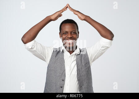 Porträt einer fröhlichen Mann hält die Hände über dem Kopf wie ein Dach Haus auf grauem Hintergrund Stockfoto