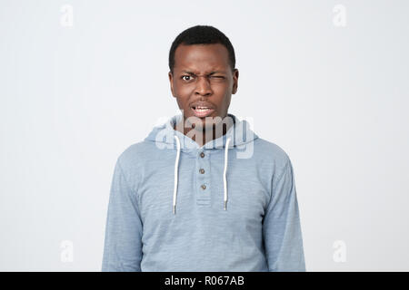 Junge afrikanische Mann im blauen Hemd mit verwirrten Ausdruck auf weißem Hintergrund. Stockfoto