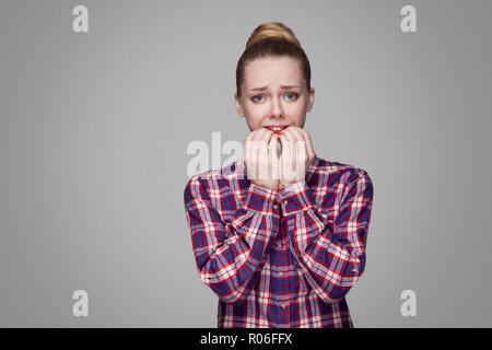 Nervös blondes Mädchen in Rot, Rosa kariertem Hemd, sammelte bun Frisur, Make-up-stehen und von der Kamera mit Panik und beißen die Zähne. indo Stockfoto