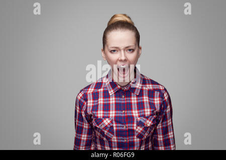 Wütend schönen blonden Mädchen in Rot, Rosa kariertem Hemd, sammelte bun Frisur, Make-up-stehen und von der Kamera mit und Schreien. indoor St Stockfoto