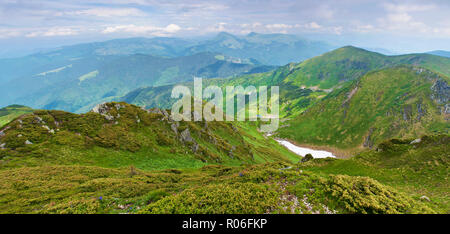 Panorama von einem Tal umgeben von majestätischen Bergen Hügel, grüne Wiesen, Wald und Schnee Reste abgedeckt. Sonnig bewölkt Tag im Sommer, im Juni. Stockfoto