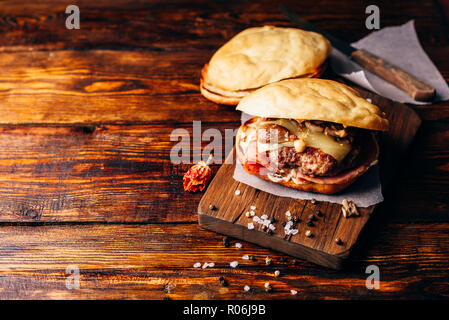 Hausgemachten Burger auf Schneidebrett. Cheeseburger mit Rindfleisch Patty, Wisconsin Schweizer Käse, Schinken, sautierten Champignons, Dijon Senf, Mayonnaise und Kartoffel R Stockfoto