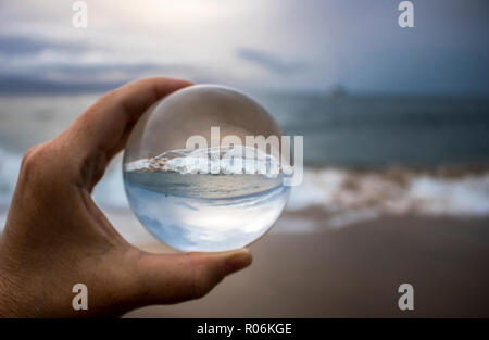 Stürmische Brandung auf Sand in Glaskugel Reflexion in der Hand gefangen gehalten brechen Stockfoto