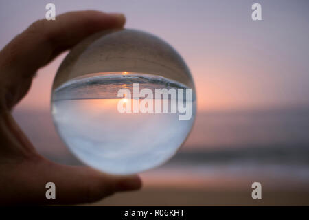 Sonnenuntergang Meereslandschaft mit Sonne am Horizont und einzigen Boot in Glaskugel Reflexion in der Hand gehalten erfasst Stockfoto