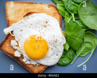 Spiegelei auf Toast und Spinat aus der Nähe von oben auf blauen Platte Stockfoto