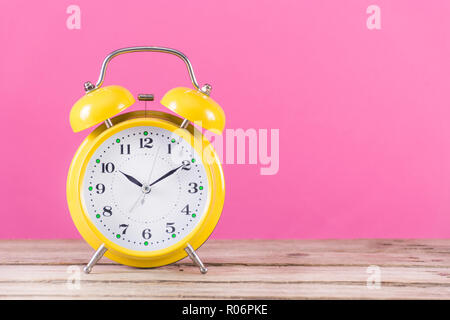 Alarm Clock auf hölzernen Schreibtisch und rosa Weiblichkeit Hintergrund. Uhr ist gelbe Farbe und mit Alarm Bell. Platz für Text und Design. Konzept