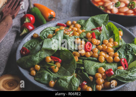 Kichererbsen und Gemüse Salat mit Spinat Blätter, gesund Hausgemachte veganes Essen, Diät. weiße Bohnen in Tomatensoße Stockfoto