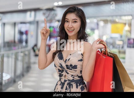 Glückliche junge Frau denken und Holding Einkaufstaschen in der Mall Stockfoto