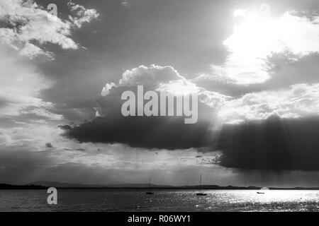 Ein paar leer, kleinen Segelboot auf einem See, unter einem Moody Himmel mit Sonnenstrahlen durch Filterung. Stockfoto