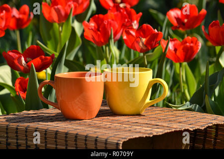 Zwei Becher mit Getränken auf einem hölzernen Serviette stand, auf dem Hintergrund der roten Tulpen. Stockfoto