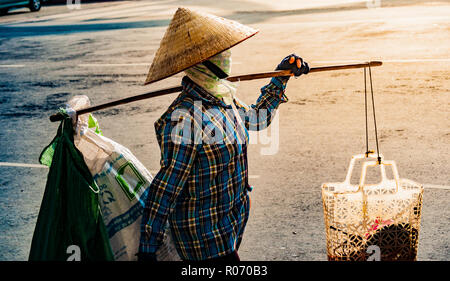 Vietnamesische mit konischen Hut trägt ein Joch auf der Schulter entlang der Straße. Stockfoto