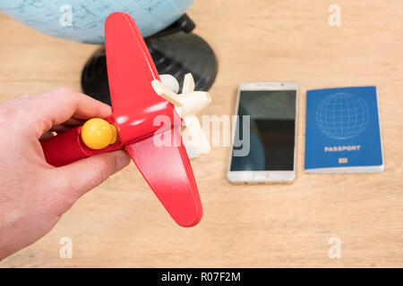 Männliche Hand spielen mit dem Flugzeug auf dem Hintergrund einer Pass-, Telefon- und Globus, stehend auf dem Tisch Stockfoto