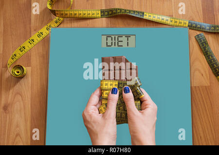 Hände von Frau mit auf die Waage um Hilfe zu bitten, die Versuchung, Süßigkeiten zu essen, zu vermeiden. Essen Sie Süßigkeiten, gesunde Ernährung Konzept mit Messung Stockfoto