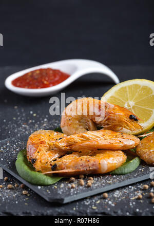 Köstlich frischer Garnelen in Butter gedünstet mit würziger Tomatensoße und Kalk auf einen schwarzen ausgefallenen Platte serviert. Kopieren Sie Platz für Text. Vertikale Stockfoto