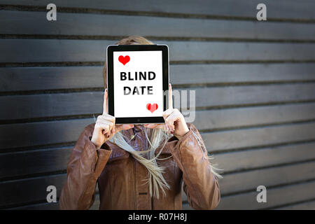 Junge Frau zum Blind Date mit Gesicht verstecken hinter Tablet mit 'Blind text' geschrieben und roten Herzen formen vorbereitet Stockfoto