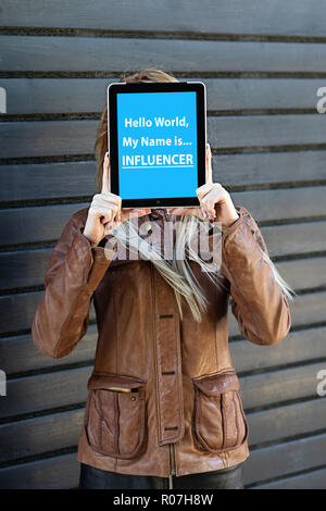 "Hallo Welt, mein Name Beeinflusser ist "Text auf Tablet in den jungen Blogger frau Hände auf hölzernen Hintergrund isoliert. Wer sind die Meinungsbildner in ihrem Leben? Stockfoto