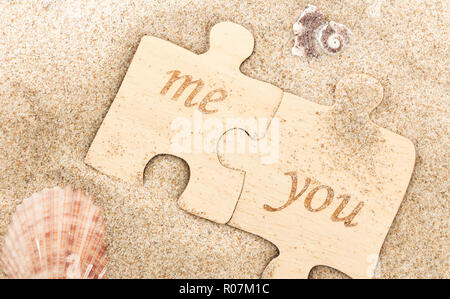 Zwei Stücke Holz- Puzzle mit Ich & Du Wörter, die auf sandigen Hintergrund mit Muscheln. Stockfoto