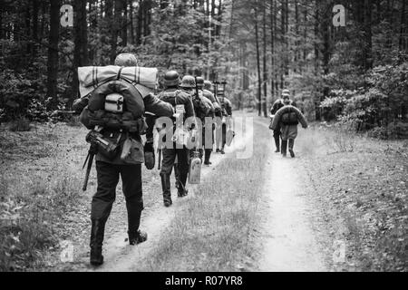 Re-enactors gekleidet, wie Deutsche Infanterie Soldaten im Zweiten Weltkrieg marschiert zu Fuß entlang der Forststraße im Sommer Tag. Foto in den Farben Schwarz und Weiß. Stockfoto