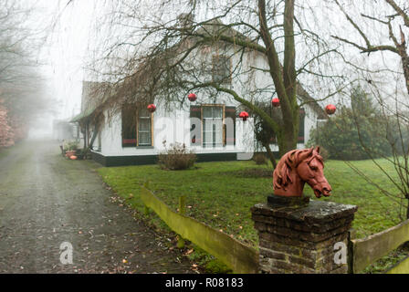 Amersfoort, Niederlande - 2018-12-16: Fahrstraße zu Weiß lackiert Bauernhaus mit roten Kugeln Weihnachten Deko und horsehead Statue Stockfoto