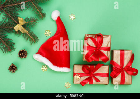 Weihnachtsdekoration. Santa's Hut, Geschenkboxen, Tannenbaum Zweige mit Zapfen und dekorative snowflackes auf grünem Hintergrund. Ansicht von oben. Weihnachten greeti Stockfoto