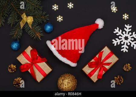 Weihnachtsdekoration. Santa's Hut, Geschenkboxen, Tannenbaum Zweige mit Zapfen und dekorative snowflackes auf schwarzem Hintergrund. Ansicht von oben. Weihnachten greeti Stockfoto