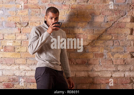 Einen selbstbewussten gutaussehenden jungen Mann trinkt Kaffee in einem Pullover. Stockfoto